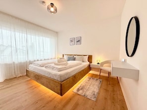 Ein modernes Schlafzimmer mit einem Holzbett, Nachttischen, einem Schreibtisch und einem großen Spiegel.