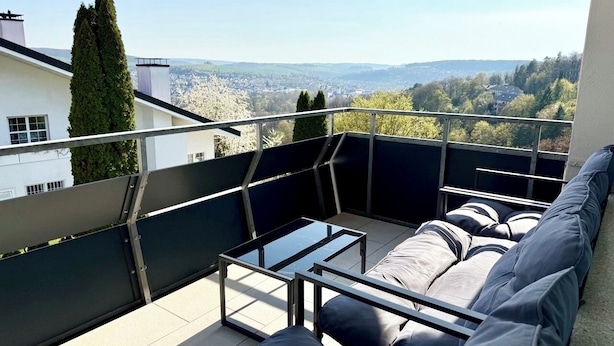 A rooftop terrace with a sofa, a glass table, and a view of a cityscape. - 3BR | parking, WLAN, home office, balcony, view, fully equipped. Kitchen (Bad Mergentheim)