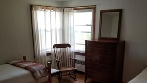 A room with two wooden beds, a wooden chair, a dresser, and a window with curtains.