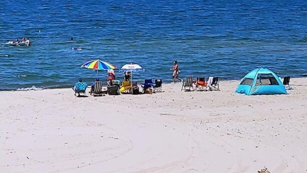 A beach with a tent, several beach chairs, and umbrellas.