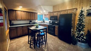 A kitchen with wooden cabinets, a black refrigerator, a stove, and a dining table with two chairs. - Serene 2-bedroom cabin on The Provo River (Provo)