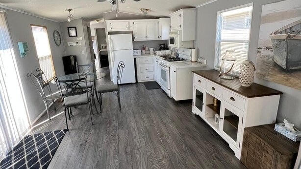 A modern kitchen with white cabinets, a dining area with metal chairs, and a ceiling fan. - Spacious Corner Lot Cottage @ Sherkston Shores (Port Colborne)