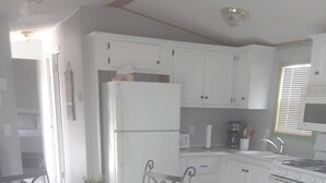 A modern kitchen with white cabinets, a stainless steel refrigerator, a gas stove, and a dining area with a glass table and metal chairs. - Spacious Corner Lot Cottage @ Sherkston Shores (Port Colborne)