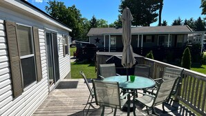 A deck with a round table and chairs, an umbrella, and a wooden railing. - Spacious Corner Lot Cottage @ Sherkston Shores (Port Colborne)