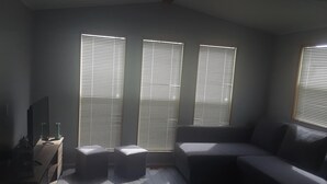 A room with a sofa, ottomans, a TV, and large windows with blinds. - Spacious Corner Lot Cottage @ Sherkston Shores (Port Colborne)