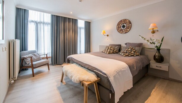 Un dormitorio moderno con una cama grande, una silla, una mesita de noche con lámpara y un reloj de pared.