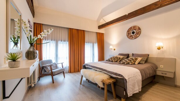 Ein Schlafzimmer mit einem Bett, Nachttischen, einem Sessel, einem Schreibtisch, einem Spiegel und einer Wanduhr.