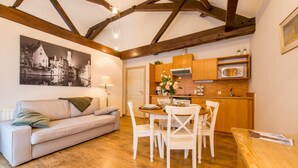 Ein gemütliches Wohnzimmer mit einer Couch, einem Esstisch und Stühlen, eine Küche mit Holdekor-Schränken und einer Mikrowelle, sowie sichtbare Holzbalken an der Decke.