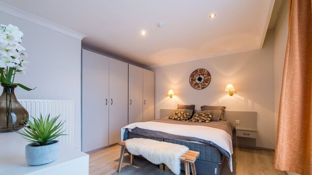 Un dormitorio con cama, mesitas de noche, un reloj y un radiador.