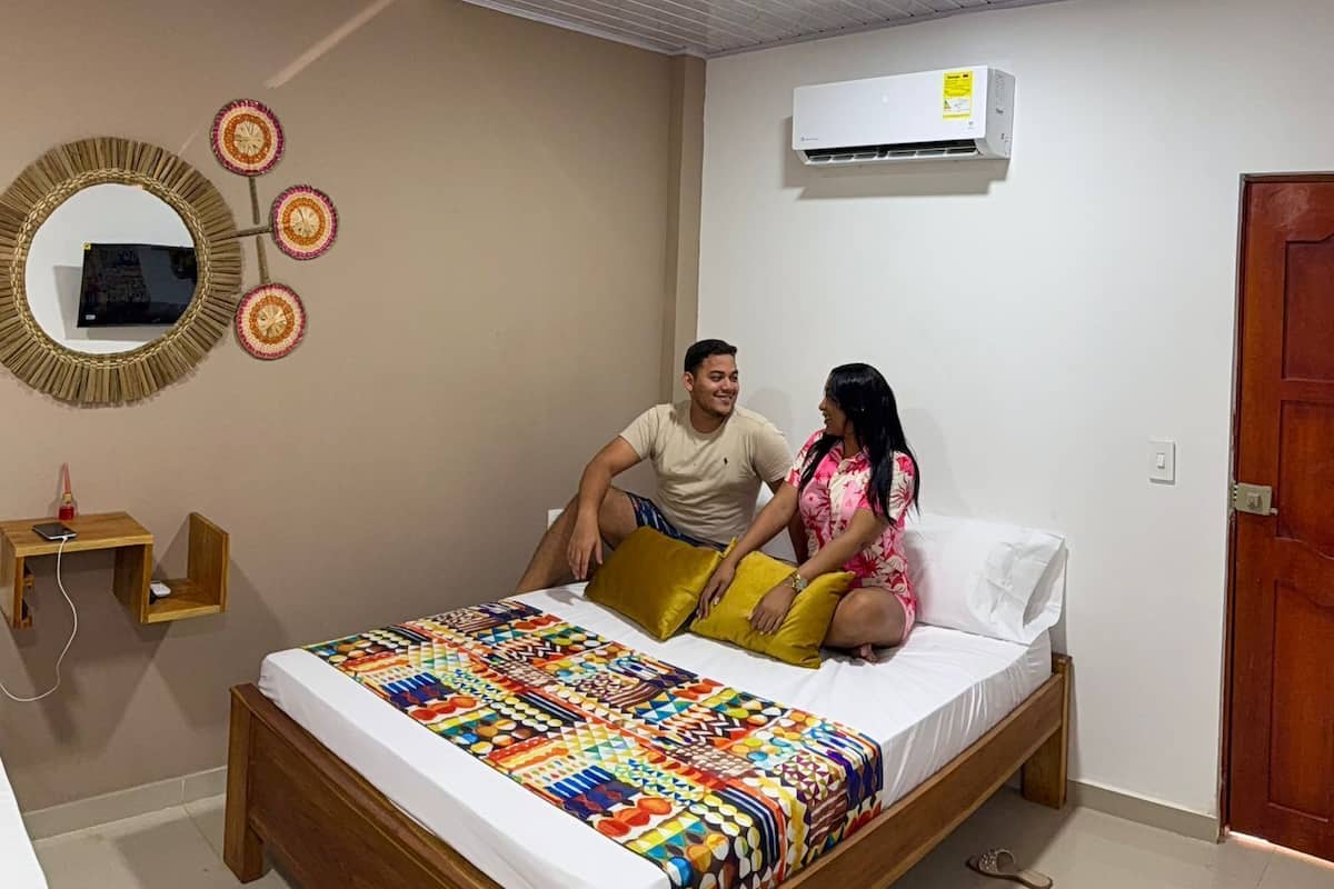 A bedroom with a bed, a wall-mounted air conditioner, a wooden nightstand, and a mirror.