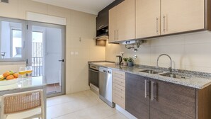 Een moderne keuken met een vaatwasser, dubbele spoelbak en een eethoek met een tafel en stoelen.