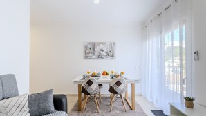 Een moderne woonkamer met een eethoek, met een bank, stoelen, een tafel met fruit en een schilderij aan de muur.