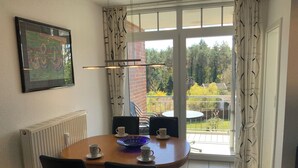 En matplats med ett bord, stolar och utsikt över en trädgård genom en glasdörr.