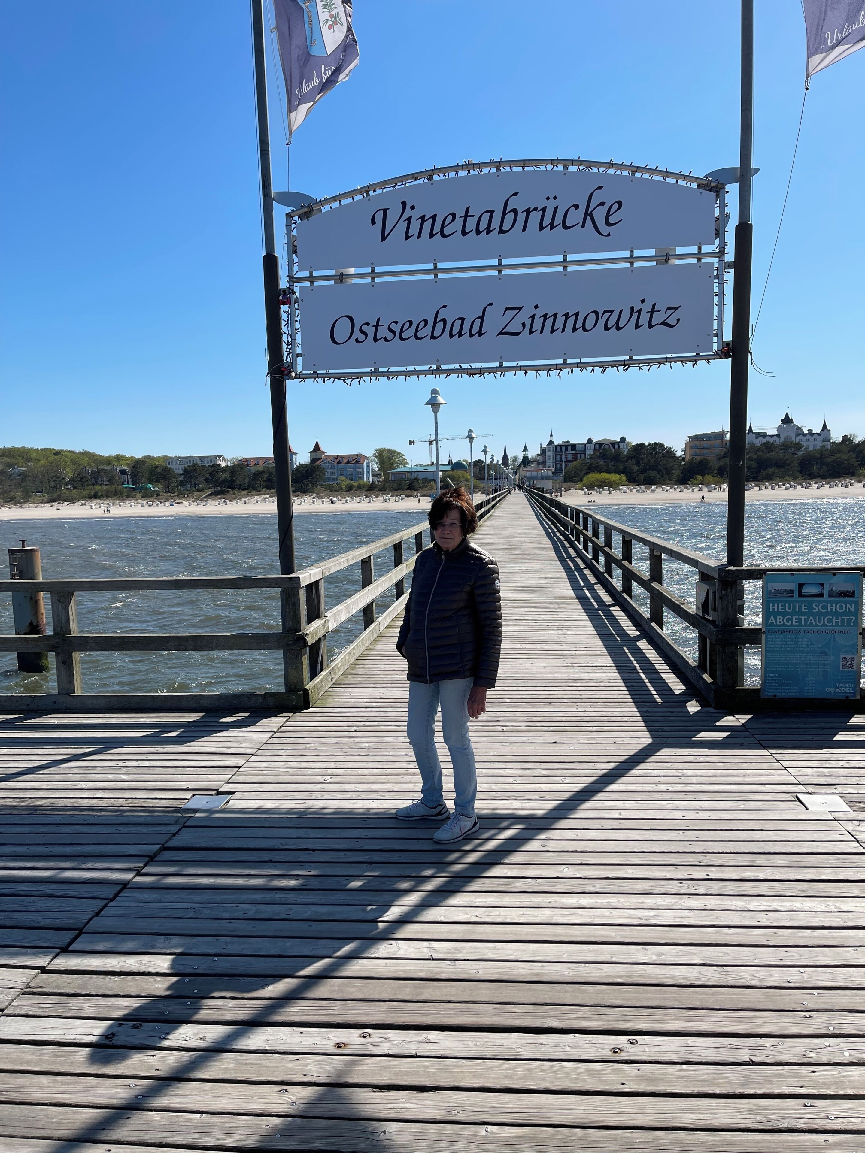 A wooden pier with a sign reading 'Vinetabrücke Ostseebad Zinnowitz' and a person standing on it.