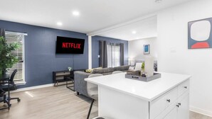 Ein modernes Wohnzimmer mit Flachbildfernseher, einer Couch, einem Couchtisch und einem Schreibtisch mit Schubladen.