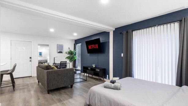 Ein modernes Hotelzimmer mit einem großen Bett, einer Couch, einem Schreibtisch, einem Fernseher und einem Fenster mit Vorhängen.