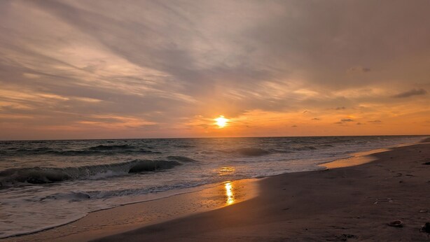 Ein Strand mit Wellen, einem Sonnenuntergang und einem klaren Himmel.