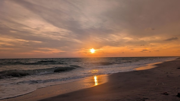 A beach with waves, a sunset, and a clear sky.