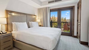 A hotel room with a large bed, a bedside table with a lamp, a window with a view of trees, and a door leading to a balcony. - Perfect condo in enchanting Aspen for your next getaway (Aspen)