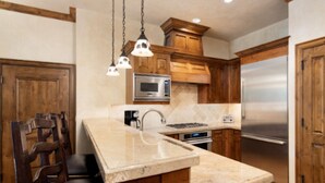 A kitchen with wooden cabinets, a marble countertop, a stainless steel refrigerator, and hanging pendant lights. - Perfect condo in enchanting Aspen for your next getaway (Aspen)