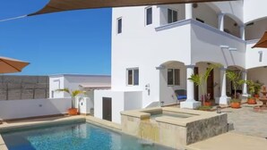 Un área de piscina con una piscina azul cristalina, un edificio blanco con balcones y plantas en macetas.