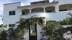 Un edificio de dos plantas con fachada blanca, un acceso cubierto y un balcón en el piso superior.