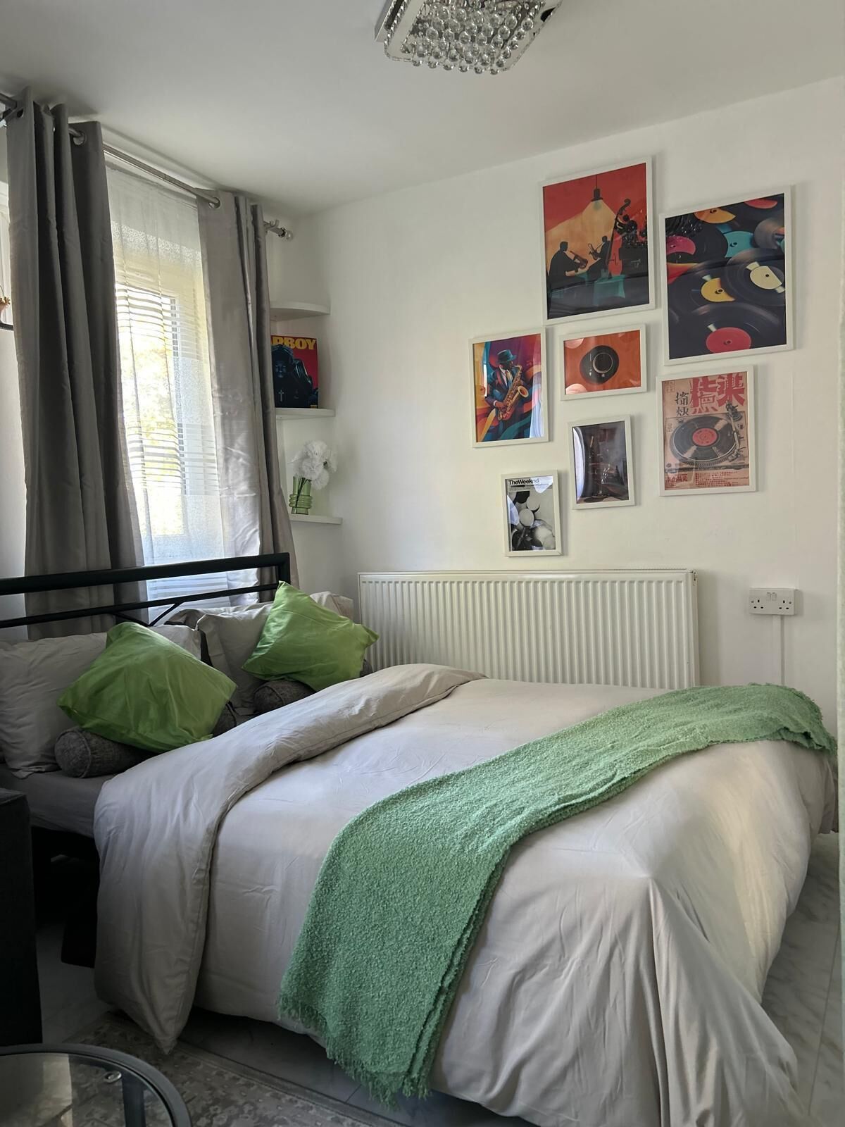 Een slaapkamer met een bed, kussens, een radiator, een raam met gordijnen en wanddecoratie.