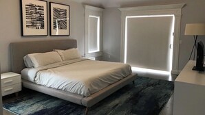 Un dormitorio con cama, mesitas de noche, lámpara y dos cuadros en la pared.