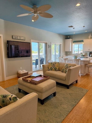 A living room with a television, a ceiling fan, and a sliding glass door leading to a balcony. - The Island Shanty (Matlacha)