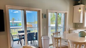 Un soggiorno con divano, una zona pranzo con sedie, una cucina con pensili e una porta scorrevole in vetro che dà su un patio esterno.