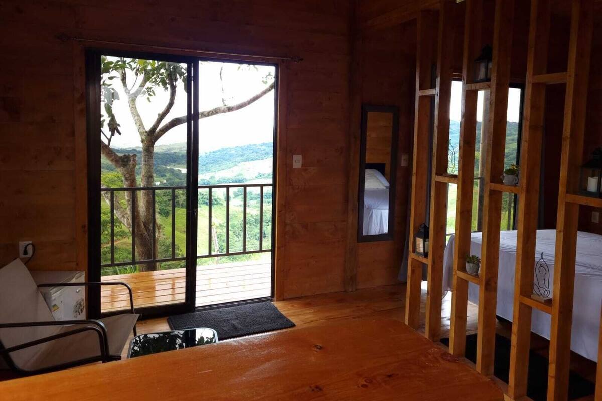 A wooden room with a large sliding glass door, a bed, a small table, and a chair.