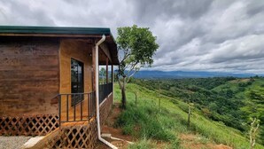 A wooden cabin with a balcony, surrounded by lush green hills and a cloudy sky. - Dulces Momentos PZ (San Pedro)