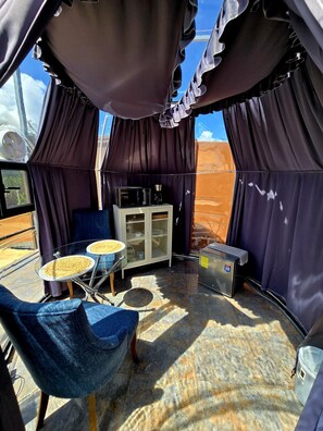 A tented area with a table, chairs, a cabinet, and a refrigerator.