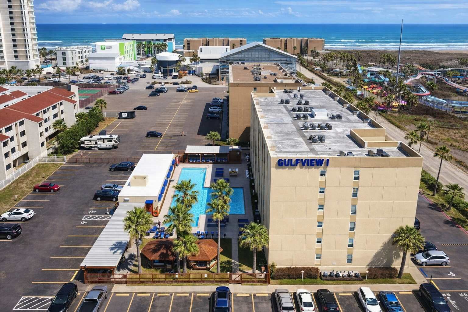 Um hotel com piscina no terraço, estacionamento e vista para a praia.