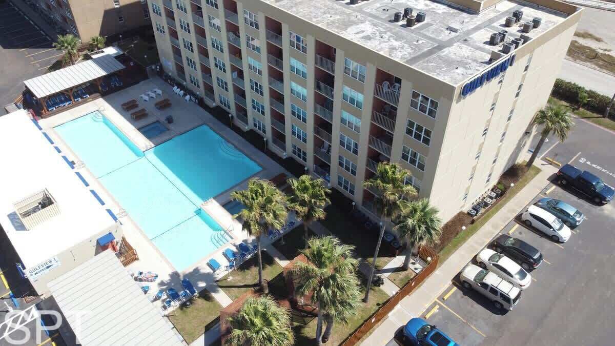 Un hotel con piscina en la azotea, varios balcones y aparcamiento.