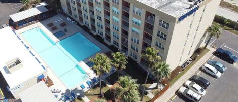 Un hotel con piscina en la azotea, varios balcones y aparcamiento.