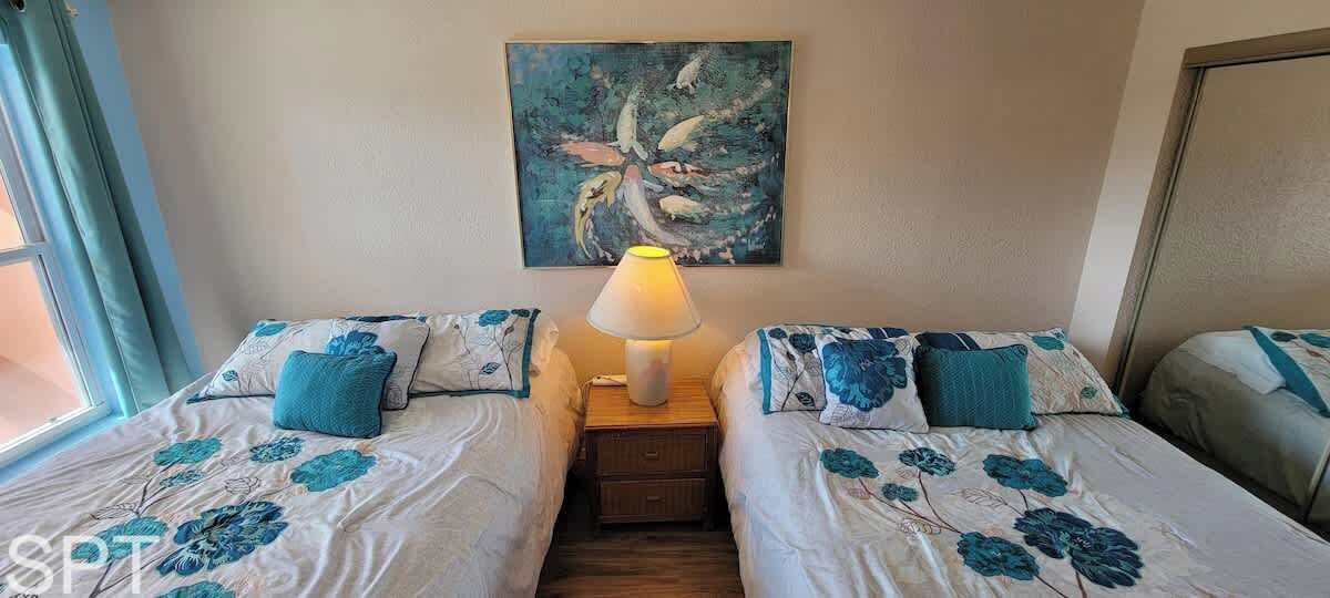 A room with two beds, each with floral bedding and matching pillows, a bedside table with a lamp, and a painting on the wall.