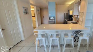 A modern kitchen with white cabinetry, a large island with bar stools, and a microwave. - Beach Access Condo - Pool - Hot Tub With BBQ (South Padre Island)