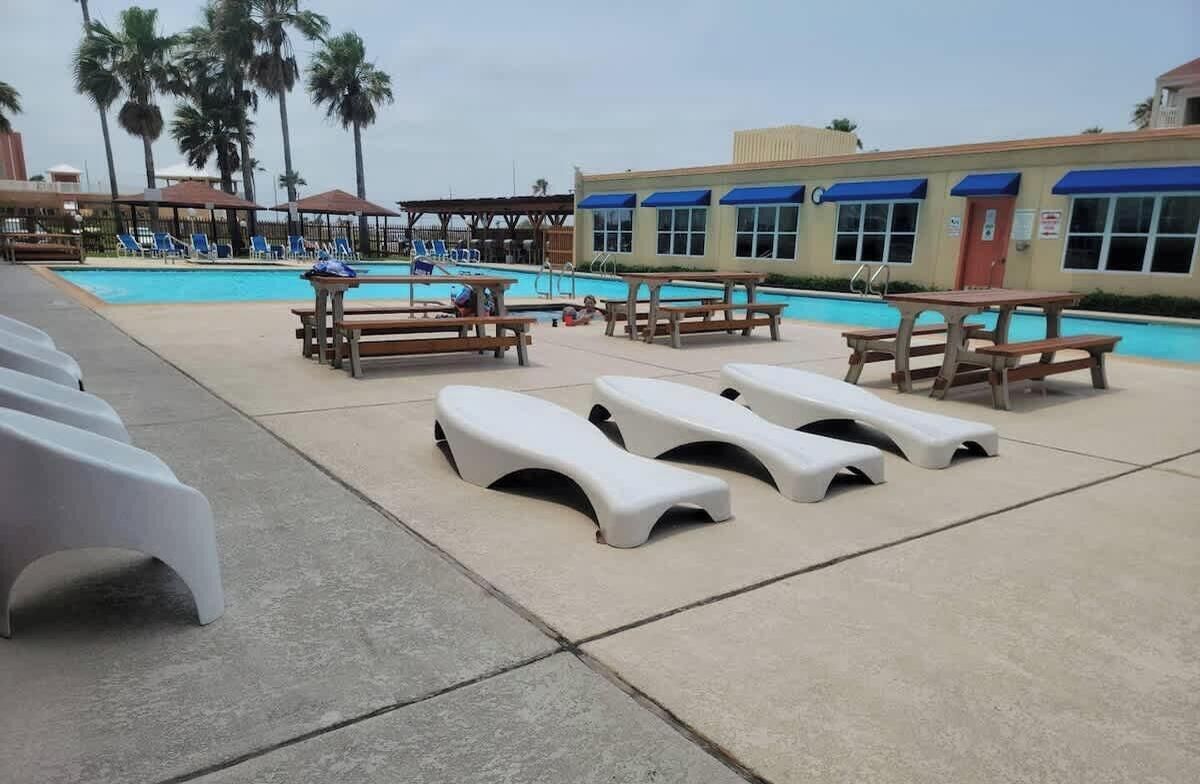 A poolside area with sun loungers, picnic tables, and lounge chairs.