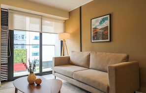 A modern hotel room with a beige sofa, a table with two vases, a floor lamp, and a large window with blinds. - w* | Amazing & Chic 1BR w/ Balcony in San Isidro (San Isidro)