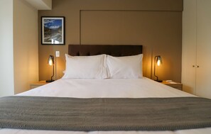 A neatly made bed with white linens, two bedside lamps, a framed picture on the wall, and a brown headboard. - w* | Amazing & Chic 1BR w/ Balcony in San Isidro (San Isidro)