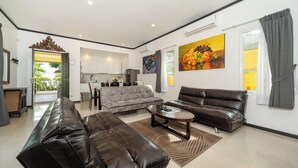 A modern living room with a sofa, a coffee table, and a dining area with a kitchen in the background. - Tropical Pool Villa with 3 Bedrooms in Rawai (Tambon Rawai)