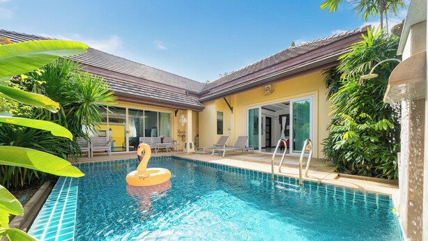 A swimming pool with a swan float, surrounded by greenery and a building with a tiled roof. - Tropical Pool Villa with 3 Bedrooms in Rawai (Tambon Rawai)