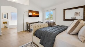 Une chambre à coucher comprenant un lit, un bureau, une chaise, une lampe sur pied et une grande fenêtre.