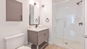 Un baño moderno con inodoro, lavamanos, espejo y ducha con mampara de vidrio.