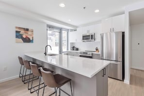 A modern kitchen with a large island, stainless steel appliances, and bar stools. - Modern Apt Near Kendall Square & Restaurants (Cambridge, MA)