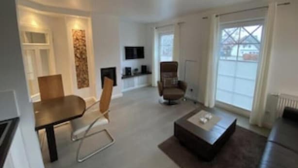 En moderne stue med spisebord, to stole, sofa, sofabord og pejs.