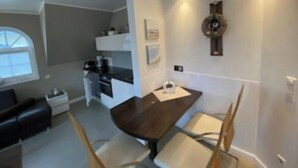 Et kompakt køkken med moderne hårde hvidevarer, et spisebord med stole, en sort sofa og et vindue.