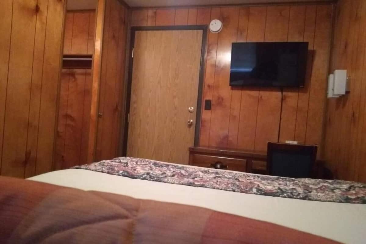 Egy hálószoba, amelyben van egy ágy, egy fa ajtó, egy televízió és egy íróasztal.