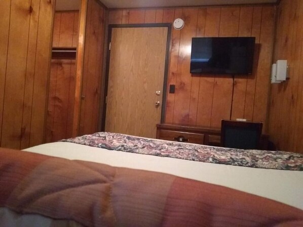 A bedroom with a bed, a wooden door, a television, and a desk. - The Orca Inn (Friday Harbor)